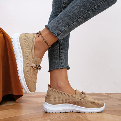 Model draagt beige stijlvolle en ademende schoenen loafers instappers met gouden detail sport schoenen dames beige witte zool