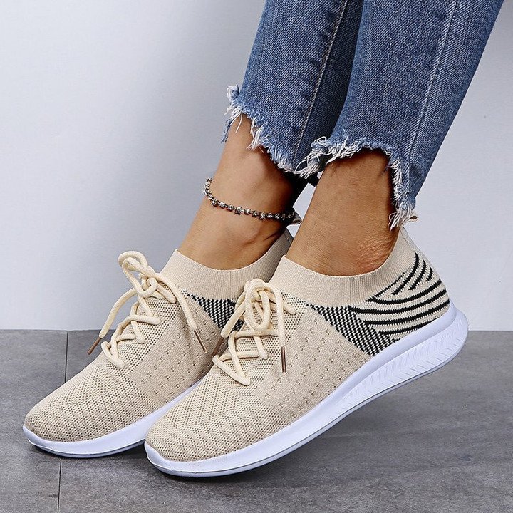 Model draagt lichtgewicht orthopedische ondersteunende dames vrouwen schoenen sneakers elastisch met witte zool en veter sluiting beige