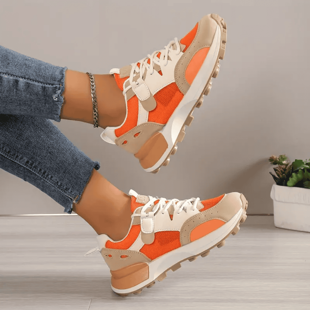 Model draagt stijlvolle modieuze orthopedische sneakers voor dames ondersteunende schoenen met elastiche sluiting oranje beige wit