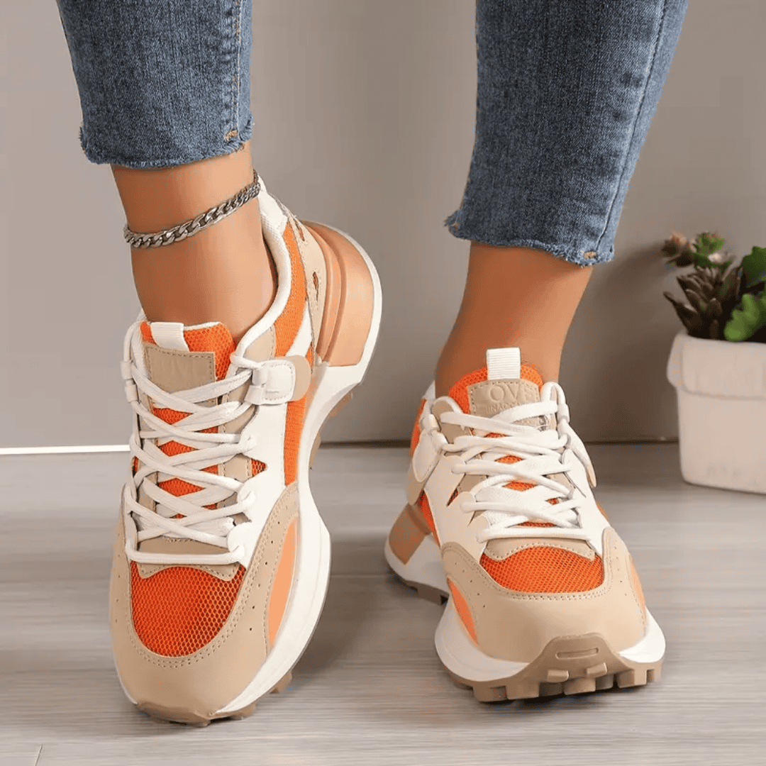 Model draagt stijlvolle modieuze orthopedische sneakers voor dames ondersteunende schoenen met elastiche sluiting oranje beige wit