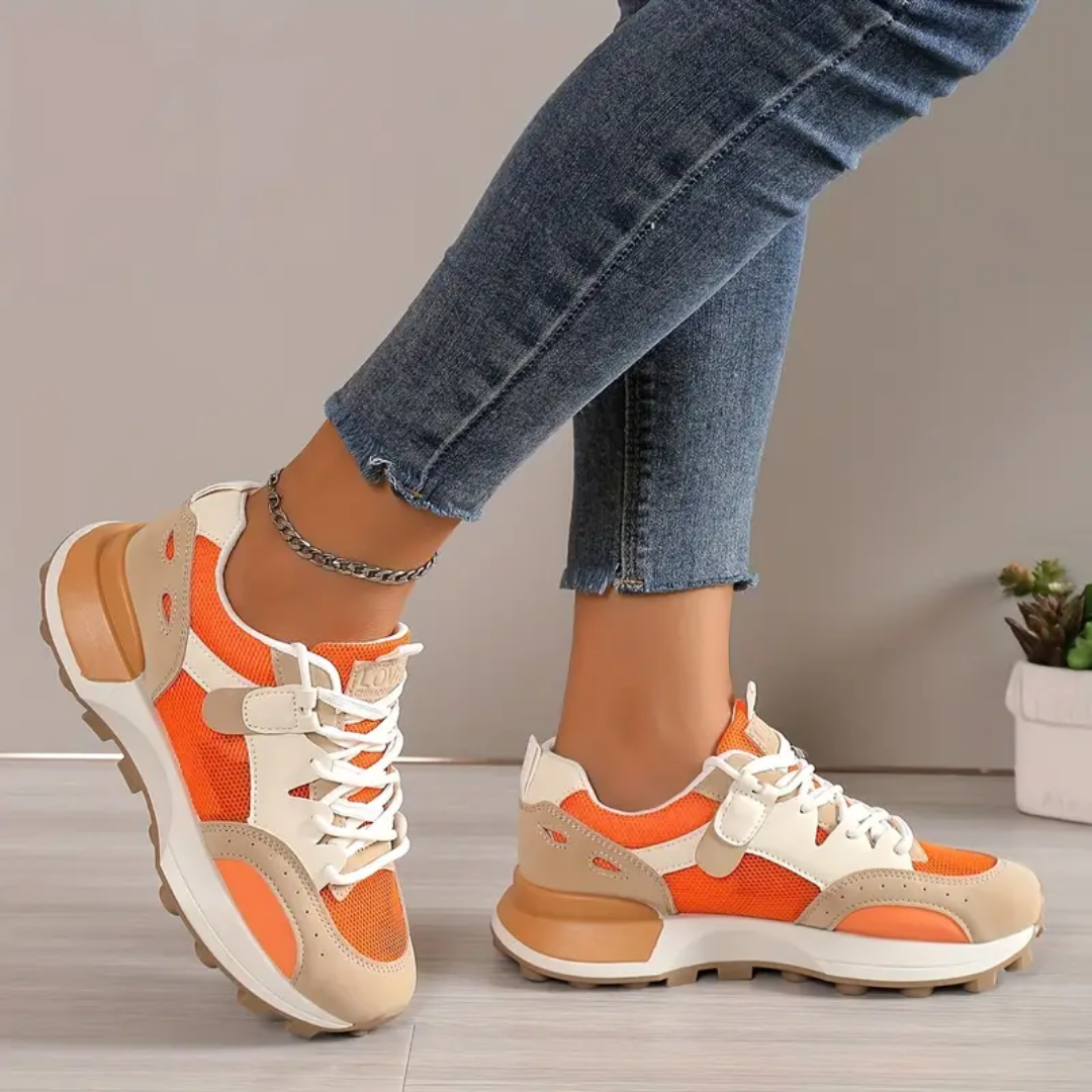 Model draagt stijlvolle modieuze orthopedische sneakers voor dames ondersteunende schoenen met elastiche sluiting oranje beige wit 