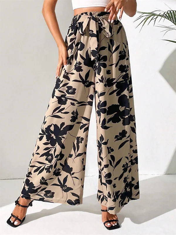 Model draagt wijde broek met bloemenprint en hoge taille losse broek linnen katoenen zomer broek dames met witte top striksluiting taille sluiting beige zwart