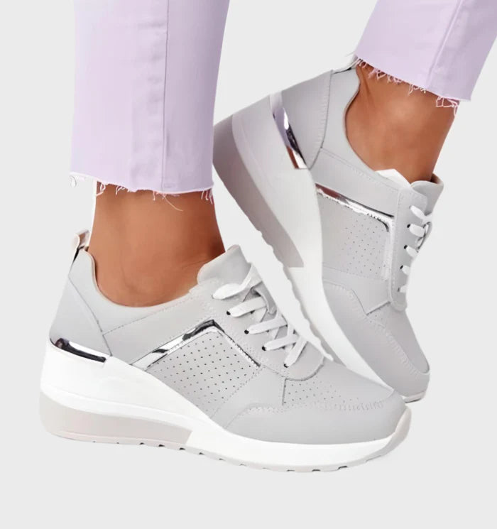 Model draagt orthopedische ondersteunende sneakers met sleehak en veter detail glimmend detail grijs