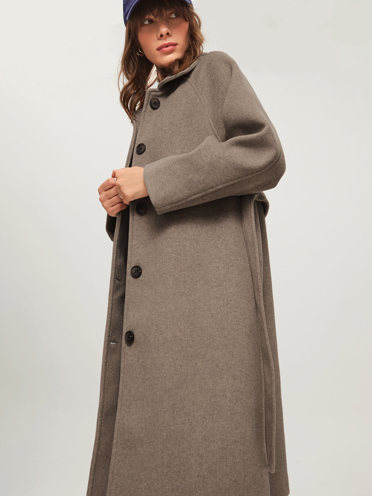 Model draagt lange cashmere trenchcoat voorjaarsjas met knoopsluiting voor en lange riem belt khaki beige