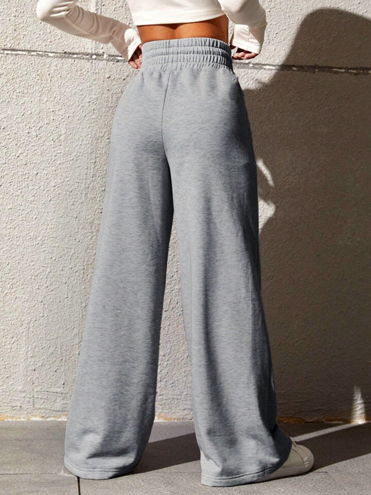 Model draagt comfortabele losse wijde joggingbroek sweatpants met brede elastische band en hoge taille met knoopsluiting streeppatroon grijs dames vrouwen