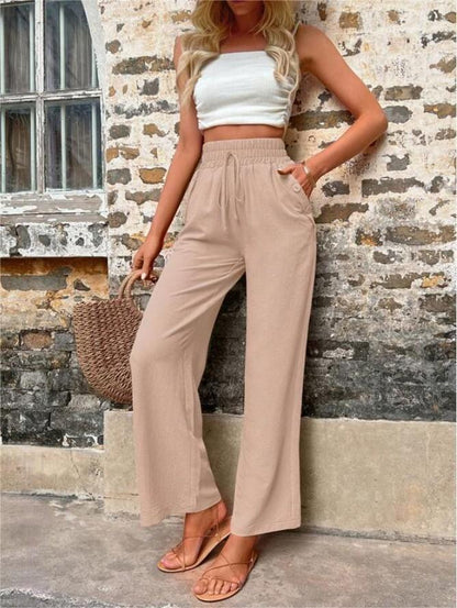 Model draagt losse comfortabele linnen broek met hoge taille en brede elastische band met verstelbare koortsluiting en knoopdetail bij de boekzak beige