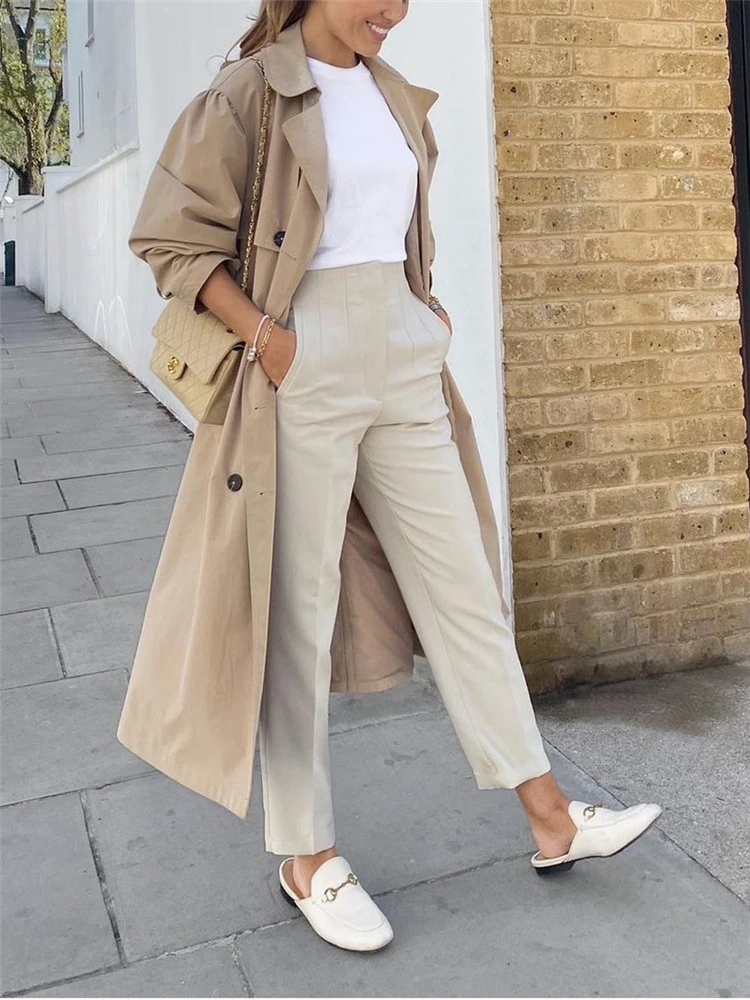Model draagt chique damesbroek met hoge taille, pakbroek broekpak dames met gevouwen details bij de heupen en broekzakken, broek heeft wijde pijpe met een dunne stof, zomerbroek linnen broek vrouwen beige