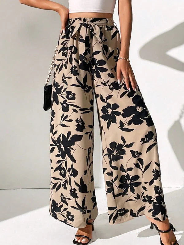 Model draagt wijde broek met bloemenprint en hoge taille losse broek linnen katoenen zomer broek dames met witte top striksluiting taille sluiting beige zwart