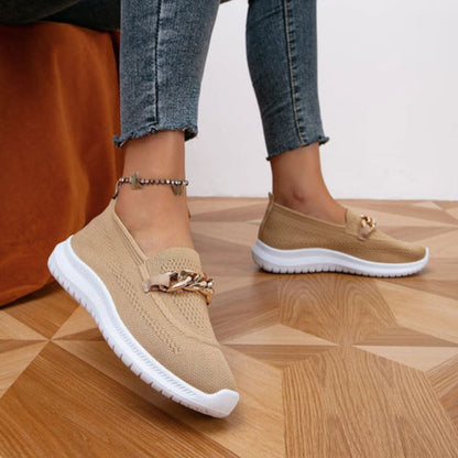 Model draagt beige stijlvolle en ademende schoenen loafers instappers met gouden detail sport schoenen dames beige witte zool