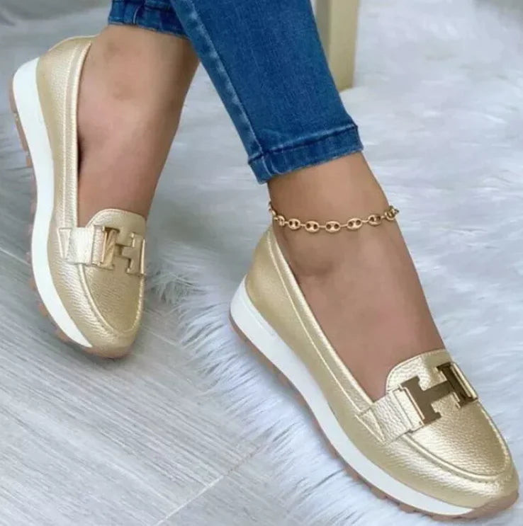 Model draagt Orthopedische loafers sneakers instappers schoenen voor dames met H logo goud